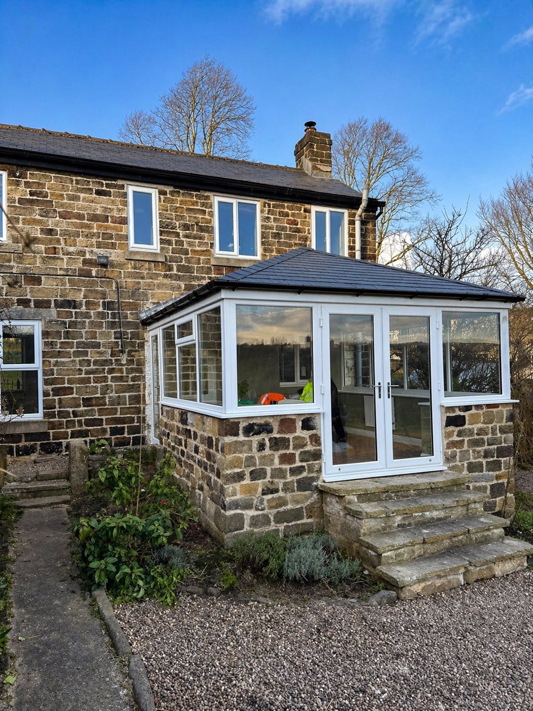 A stone cottage with a conservatory fitted with a dark tiled warm roof