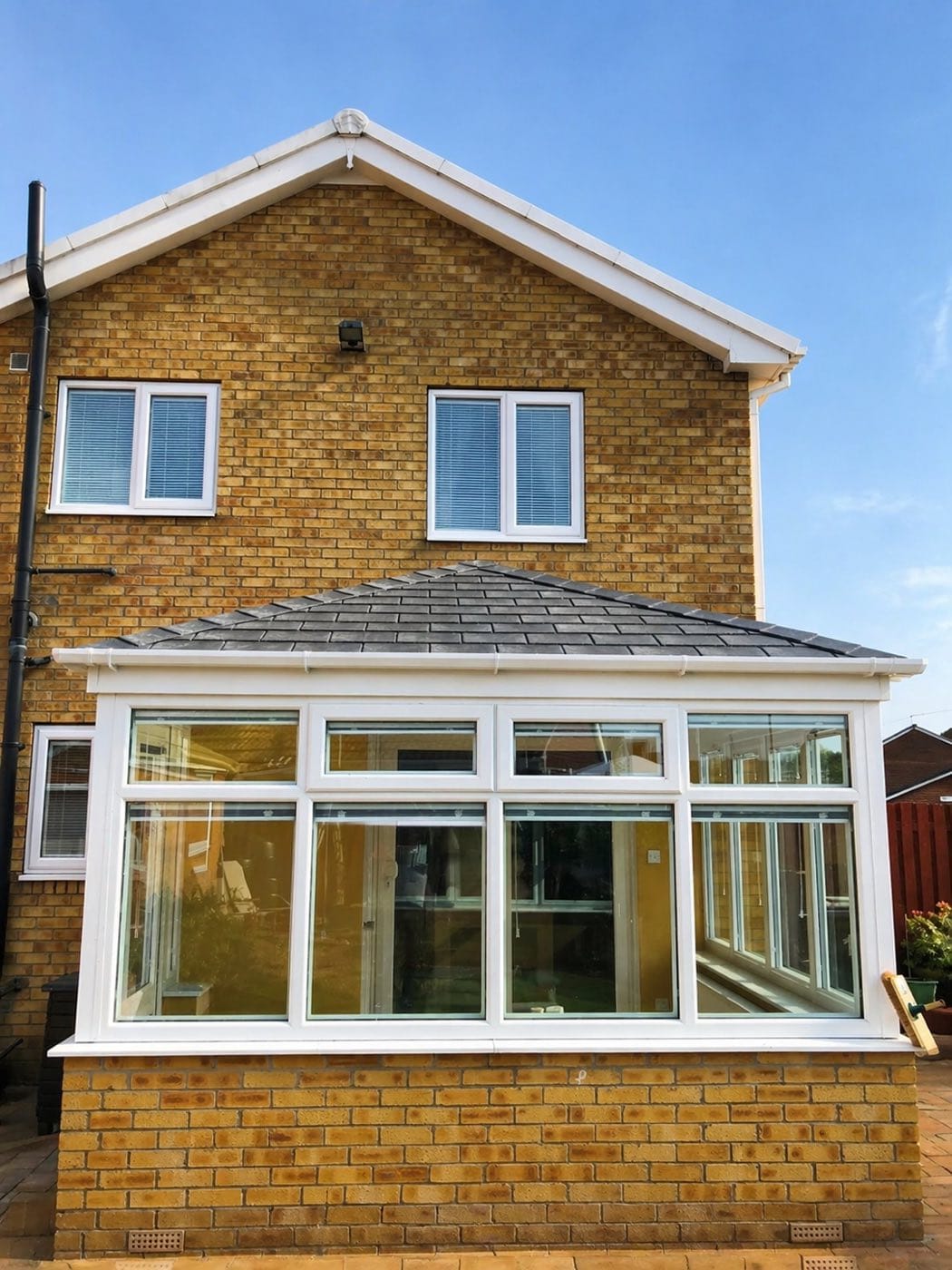 A conservatory with a grey tiled warm roof fitted to a buff brick house