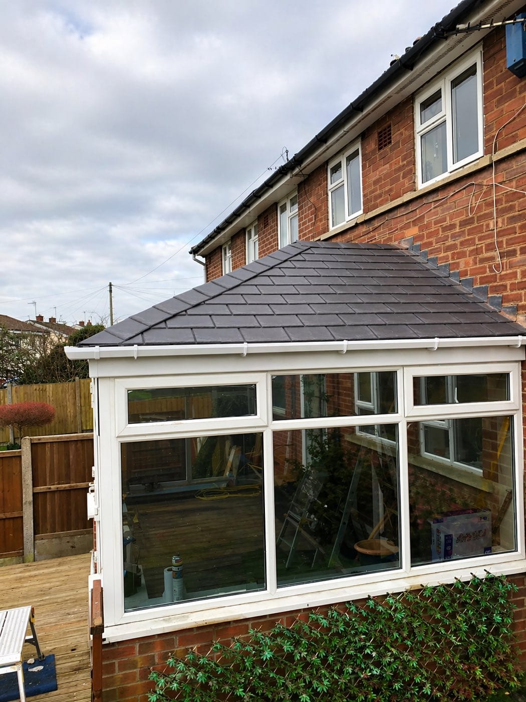 A conservatory with a completed slate grey tiled warm roof, fitted against a red brick house