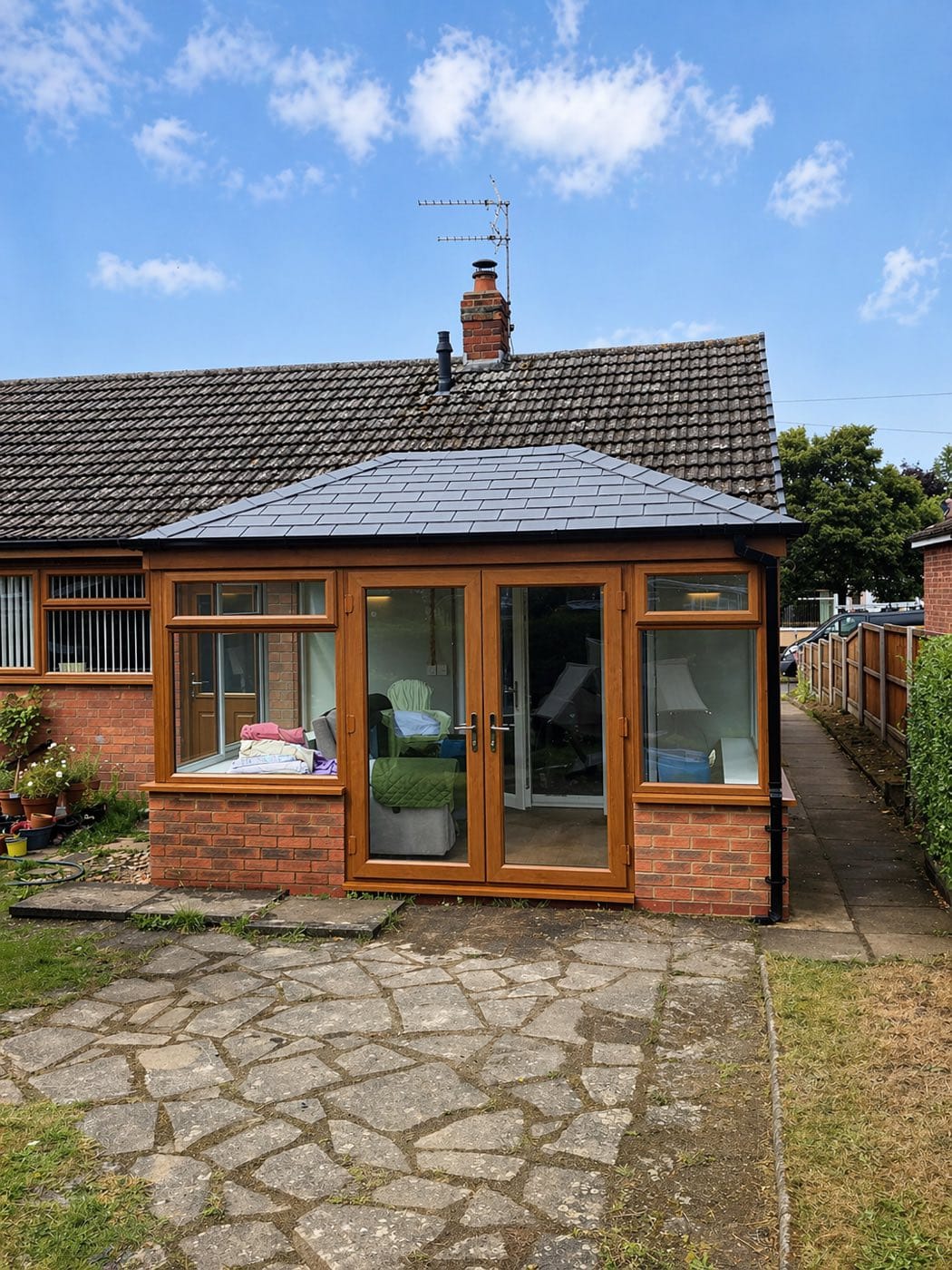 A conservatory on a bungalow with a slate grey tiled warm roof and golden oak frames